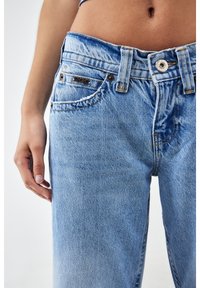 Jeans de mezclilla azul claro con una cintura alta, presentan un cierre frontal con botón y un ligero desgaste en los bolsillos y costuras.