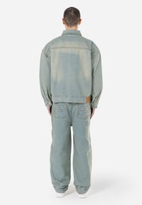 Svijetloplava denim jakna i hlače. Opustiti kroj s laganim izbljeđivanjem, vidljivim šavovima i logotipima na džepovima.