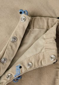 Bež kordurovina s podlogo, ki vsebuje srebrne sponke in modre vezenine. Gladek tekstura in rahlo rebrasta vzorec.