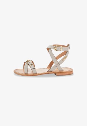Sandal plat avec des brides en cuir gris, design croisé, accents en boucle en métal doré, et une semelle intérieure texturée de couleur brun clair.
