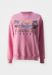 Pink crewneck sweatshirt featuring a graphic design of a sunset, palm trees, and a sailboat with "Panama Bay" text. Soft fabric texture.