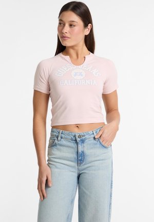 Ružový skrátený tričko s okrúhlym výstrihom, krátkymi rukávmi a svetlomodrým logom "Guess Jeans California". Nosí sa s svetlomodrými džínsami.