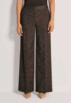 Pantalon large brun foncé texturé, porté avec des chaussures beiges pointues et un haut noir, montré de la taille aux pieds.