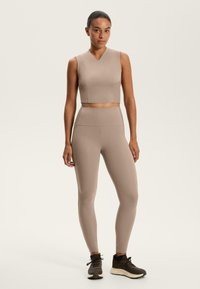 Top corto beige con scollo a V e design senza maniche, abbinato a leggings a vita alta dello stesso colore. Tessuto liscio e forma aderente.