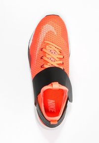 Sneakers Nike con una vivace tomaia in tessuto arancione decorata con un motivo triangolare, una cinghia nera nella zona mediale del piede e lacci rosa.