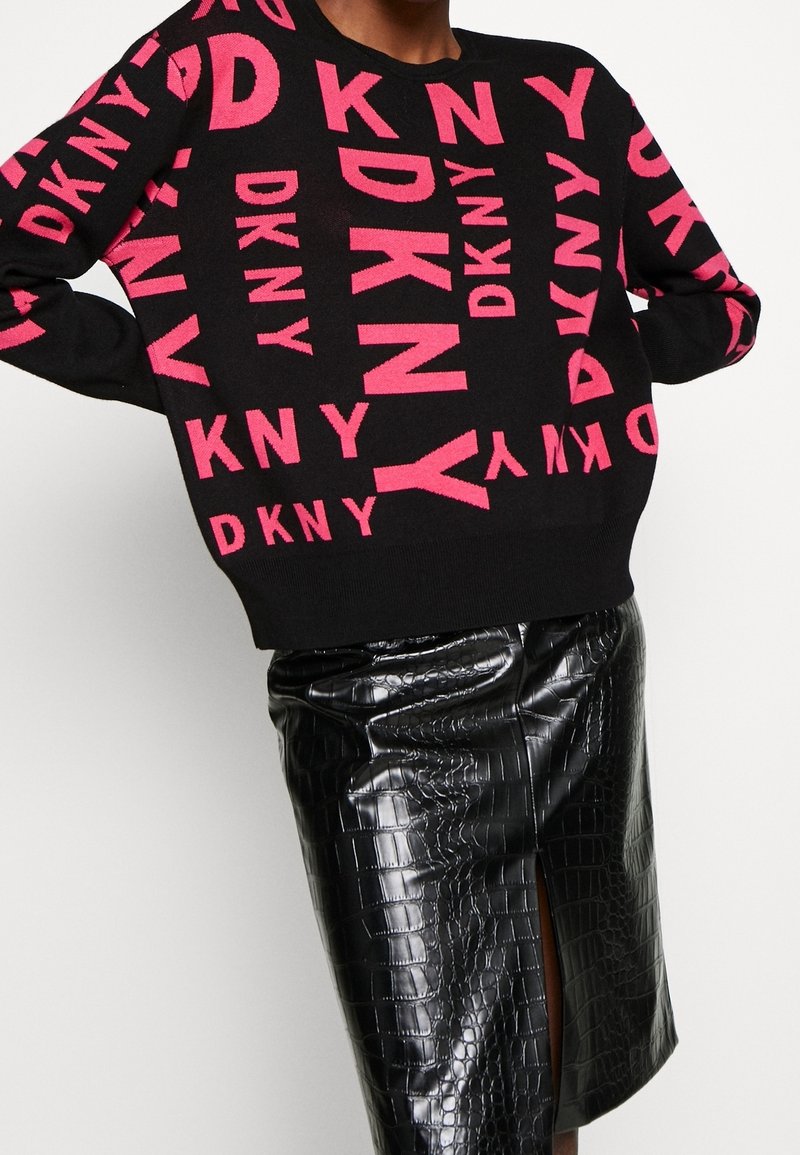 Pull noir avec un lettrage rose vif "DKNY", coupe décontractée, manches longues. Associé à une jupe noire brillante à motif crocodile.