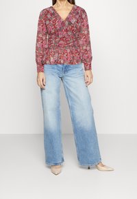 Haut à imprimé floral avec des manches longues, décolleté en V et taille smockée ; associé à un jean en denim délavé à jambe large et des escarpins nude.