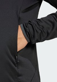 Black long-sleeve shirt with a textured surface, featuring a side pocket and fitted cuffs with a contrasting gray trim.