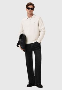 Bílý pletený polo svetr s límcem, tmavě šedé široké džíny, černé sluneční brýle a černá Messenger taška s popruhem.