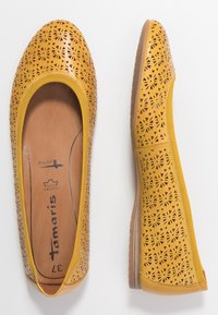 Bailarinas amarillas perforadas con cortes en forma de flor, punta redondeada y suela de goma marrón flexible, con un interior de cuero.