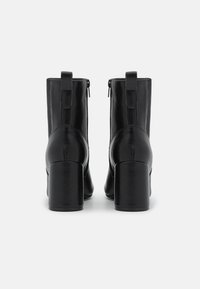 Schwarze Leder-Stiefeletten mit quadratischen Absätzen, ausgestattet mit einem Reißverschluss und Schlaufen-Ziehpullern an der Rückseite. Glatte Textur, minimalistisches Design.