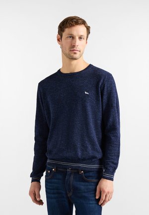 Marineblå strikket sweater med lange ærmer, rund halsudskæring og et lille hvidt logo. Har et tekstureret stof og stribede manchetter.