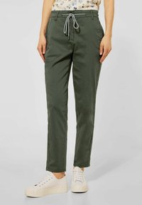 Khaki green casual pants with a drawstring waistband and side pockets, featuring a slim fit and lightweight fabric, paired with white sneakers.