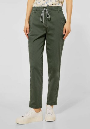 Pantalons décontractés verts kaki avec une taille élastique et des poches latérales, présentant une coupe ajustée et un tissu léger, associés à des baskets blanches.