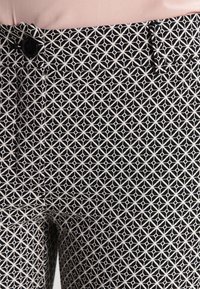 Zwart-wit gestreepte broek met een geometrisch ontwerp. Gemaakt van stof, voorzien van een knoopsluiting en een platte tailleband.