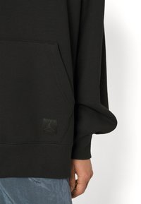 Sudadera negra con bolsillo frontal, fabricada con un tejido texturizado y con un parche negro del logo Jordan en el dobladillo. La manga tiene un ajuste holgado.