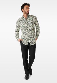 Long-sleeve button-up shirt featuring a dollar bill print in green and black on a light background, paired with black pants and shoes.
