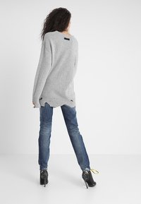 Pull gris en maille avec une coupe décontractée, ourlet côtelé et bords bruts ; associé à un jean bleu clair et des chaussures noires à talons hauts.