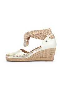 Espadrille blanche à talon compensé avec une finition dorée métallique, une semelle en corde tressée et une bride de cheville en cuir beige. Elle présente des bords festonnés et une couture décorative.