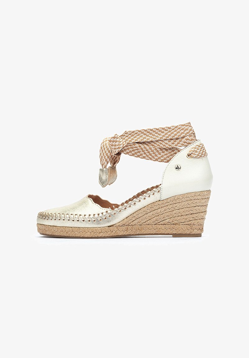 Espadrille blanche à talon compensé avec une finition dorée métallique, une semelle en corde tressée et une bride de cheville en cuir beige. Elle présente des bords festonnés et une couture décorative.