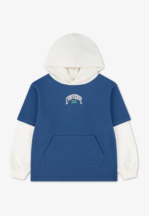 Blauer kurzärmeliger Hoodie, getragen über langen weißen Ärmeln, mit Fronttasche und dem Text ""Converse 1908"" auf der Brust.