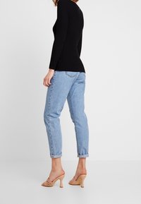 Black ribbed long-sleeve top paired with light blue tapered jeans and nude open-toe heeled mules, presented from a side angle.