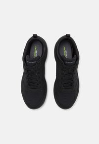 Svarta träningsskor med mesh-paneler och snören, med "Skechers Memory"-logotyp på innersulan, visade uppifrån.