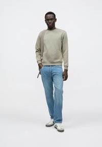 Felpa verde chiaro con collo a coste, abbinata a jeans blu slavato a gamba dritta. Sneakers grigie e bianche completano l'outfit.