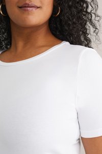 Hvid bomulds t-shirt med rund hals og korte ærmer, der har en glat tekstur og en tætsiddende silhuet. Guld hoopsøreringe synlige.
