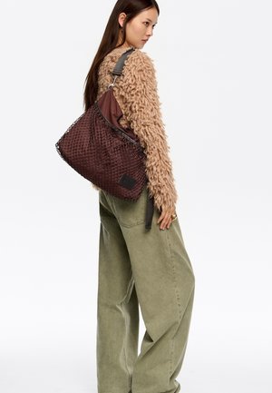 Bolso marrón tejido con un diseño de malla texturizada y un interior marrón contrastante. Cuenta con una correa para el hombro y un pequeño parche con el logo.