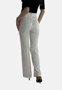 Witte tailormade broek met een hoge taille, voorzien van een gladde textuur, voorplooien en een slim-fit ontwerp. Afwerkingsdetails zijn een knoop- en ritssluiting.