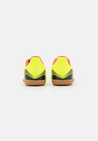 Neon yellow athletic shoes with red accents, textured upper, black detailing, and a rubber gum sole featuring a pattern for traction.