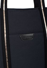 Zwarte stoffen tas met textuur en een metallic gouden streep. Heeft een zwart leren label met de naam "Hexagona" aan de voorkant.