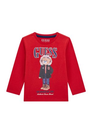T-shirt rosso a maniche lunghe in cotone biologico, con una grafica di un orso in giacca e stivali, accompagnata da testo "GUESS" in lettere grasse.