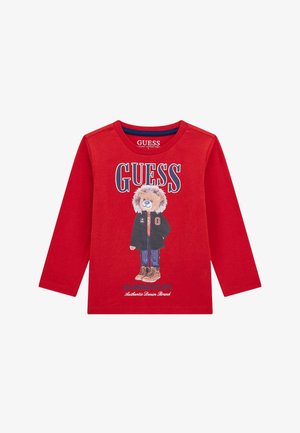 Rotes Langarm-T-Shirt aus Bio-Baumwolle, mit einem Grafikdesign eines Bären in einer Jacke und Stiefeln, mit dem Schriftzug "GUESS" in fetten Buchstaben.