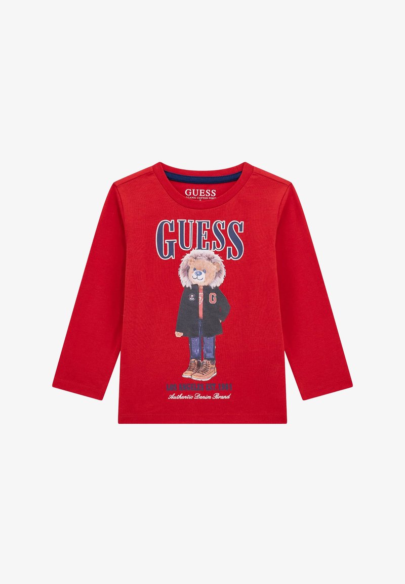 Piros, hosszú ujjú póló, organikus pamutból készült, egy kabátban és csizmában lévő medve grafikájával, a "GUESS" felirattal vastag betűkkel.