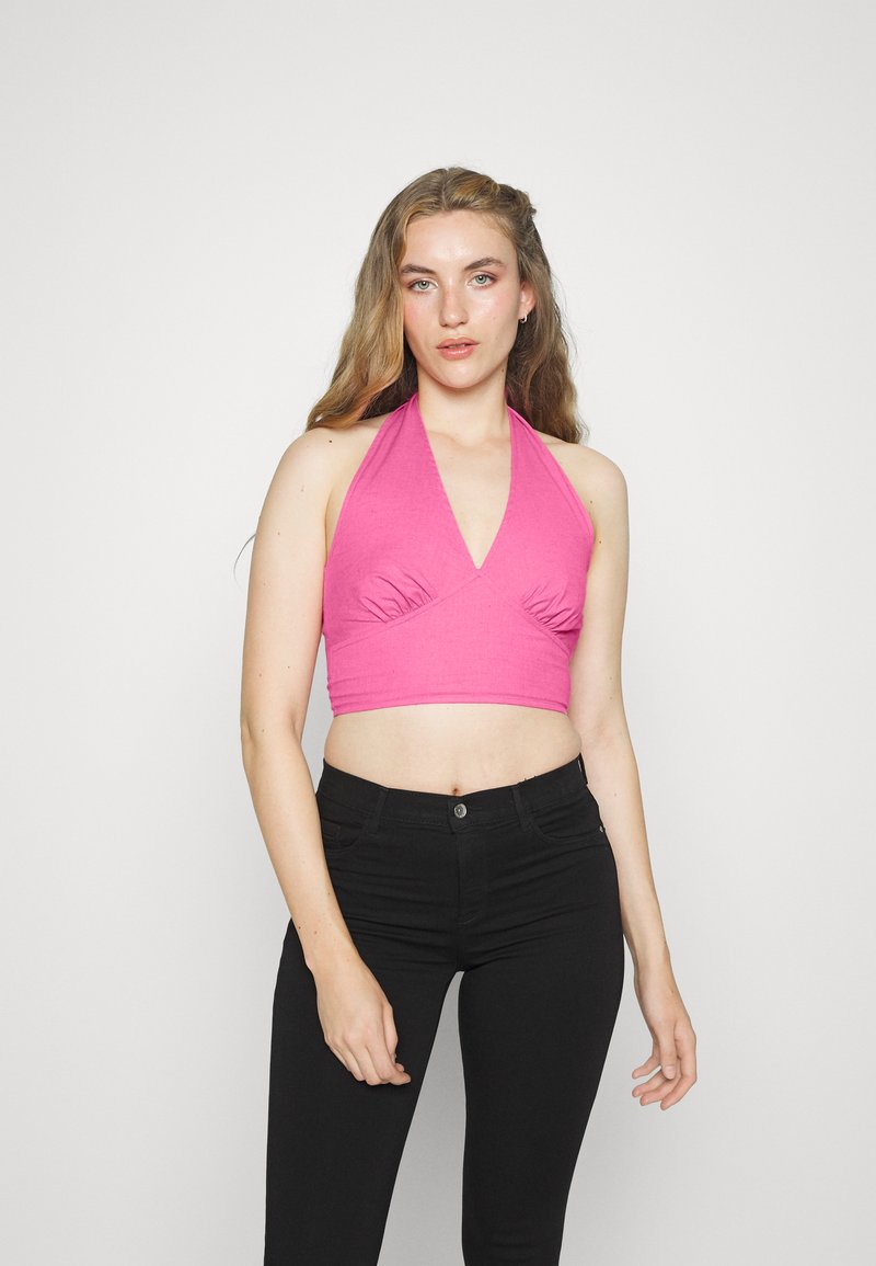 Top crop halter rosa com decote em V profundo e detalhe de franzido, combinado com jeans pretos de cintura alta. Textura de tecido suave.