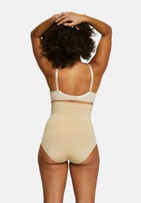Shapewear beige senza cuciture con vita alta e spalline regolabili, caratterizzato da una texture liscia e una chiusura con gancio e occhio sul retro.
