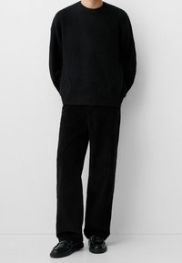 Black knitted sweater with a crew neckline, paired with black corduroy pants and black shoes. Textured fabric and relaxed fit.