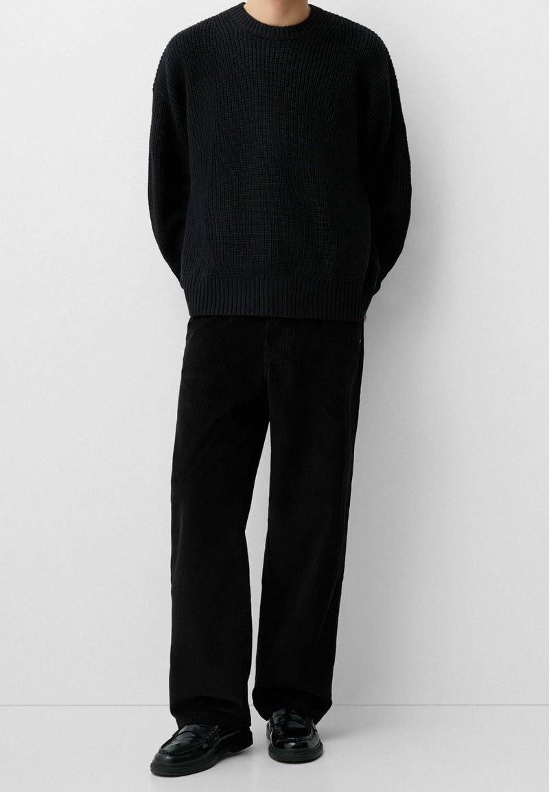 Black knitted sweater with a crew neckline, paired with black corduroy pants and black shoes. Textured fabric and relaxed fit.