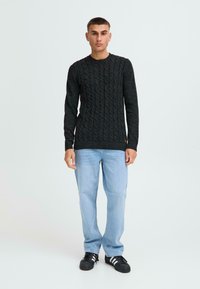 Donkergrijze gebreide trui met kabelpatroon, ronde hals en geribde manchetten, gecombineerd met lichtblauwe jeans en zwarte sneakers.