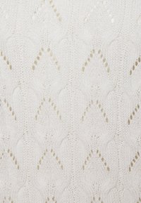 Weißer gestrickter Stoff mit einem sich wiederholenden Rautenmuster, das offene Details und eine weiche Textur aufweist.