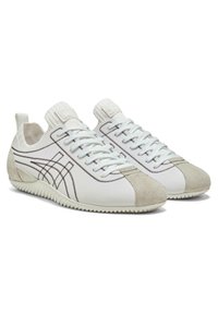 White sneakers with a suede toe cap and contrasting stitching. Features a textured, ribbed collar and flexible rubber sole.