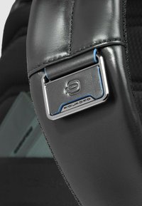 Cinturino in pelle nera con ferrature in argento lucido, caratterizzato da un accento blu. Superficie lavorata e dettaglio del logo distintivo visibile.