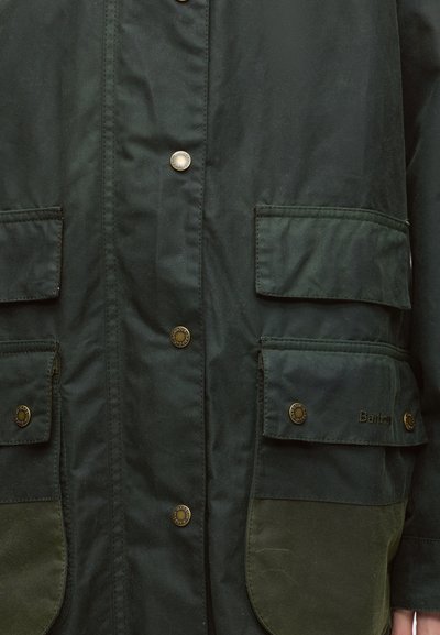 Veste vert foncé à l'avant avec quatre poches à rabat, boutons-pression en métal et nom de marque Barbour visible sur la poche inférieure droite.