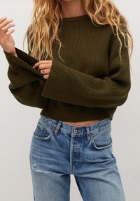 Olijfgroene geribbelde cropped trui met brede mouwen, gecombineerd met vervaagde blauwe high-waisted jeans met versleten details en een knoopsluiting.
