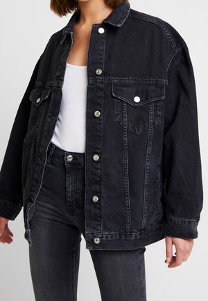 Personne portant une veste en jean noire ample par-dessus un débardeur blanc et un jean en jean noir coupé à mi-hauteur.