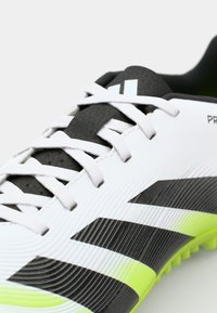 B baskets blanches avec des accents noirs et jaune néon. Présente un dessus texturé, un design à trois bandes bien visible et des lacets plats.