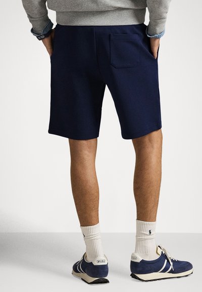 Granatowe spodenki z tylną kieszenią, noszone z szarą bluzą i niebieskimi trampkami. Akcesoria to kremowe skarpetki oraz bransoletka.