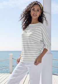 Gestreifter leichter Baumwollpullover in Weiß und Marineblau, mit einem Bootsausschnitt und Dreiviertelärmeln, kombiniert mit weißen Hosen.
